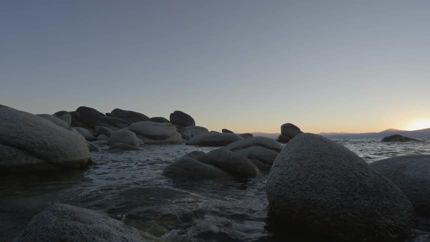 Water splashes against the rocks at sunset