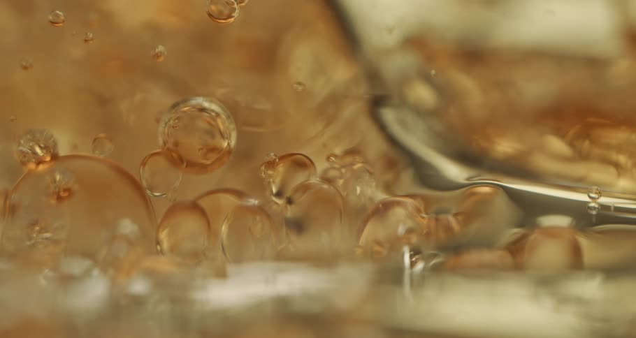 Clear liquid hits a gold surface and splashes around with bubbles