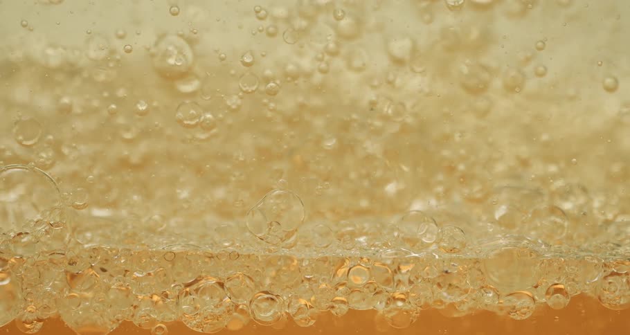 Bubbles float and rise as they move in a clear yellow liquid