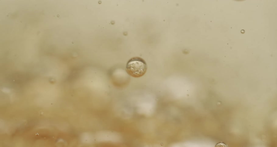 Orbs and bubbles float and move through a clear yellow liquid