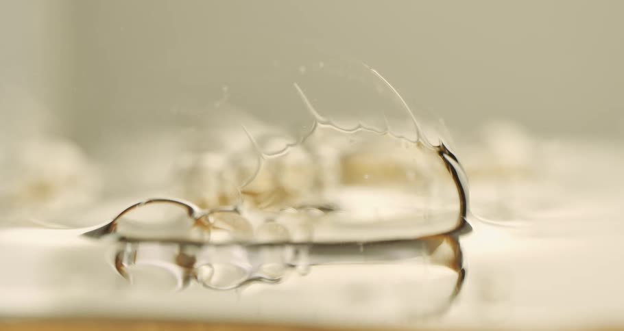 Close up view of a bubble as it pops and shrinks into the wet surface