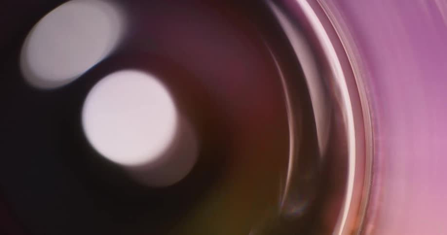 Colorful spinning lights reflect and flare on a lens against a black background