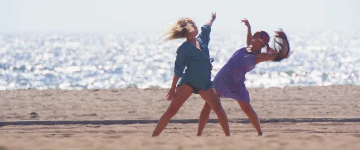 Two women on the sand of a beach dancing together