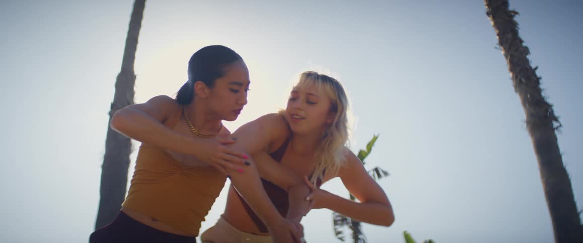 Two women dancing outdoors next to trees and vegetation during day time