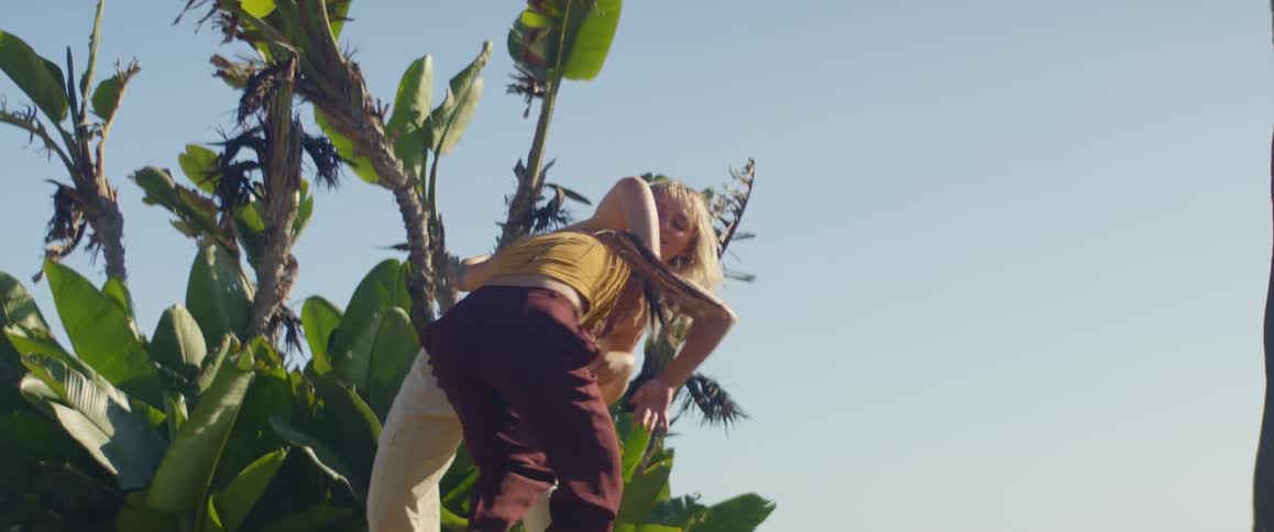Two women perform a choreographed dance in front of plants