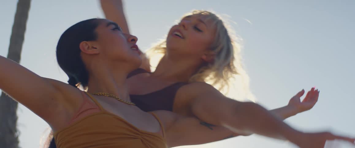 Two woman dance while sitting in the sun outdoors entangling the their arms and self close together
