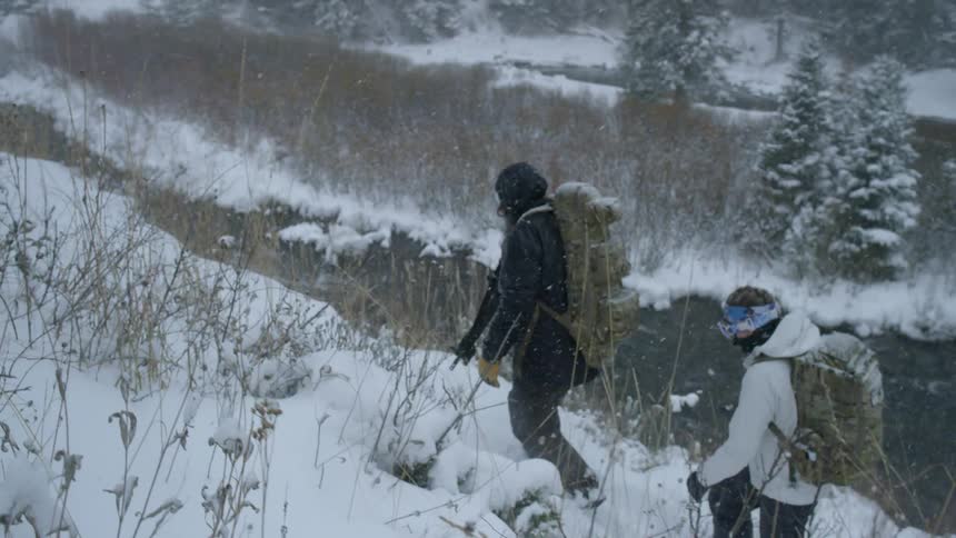 Two people hike on a hill as it snows