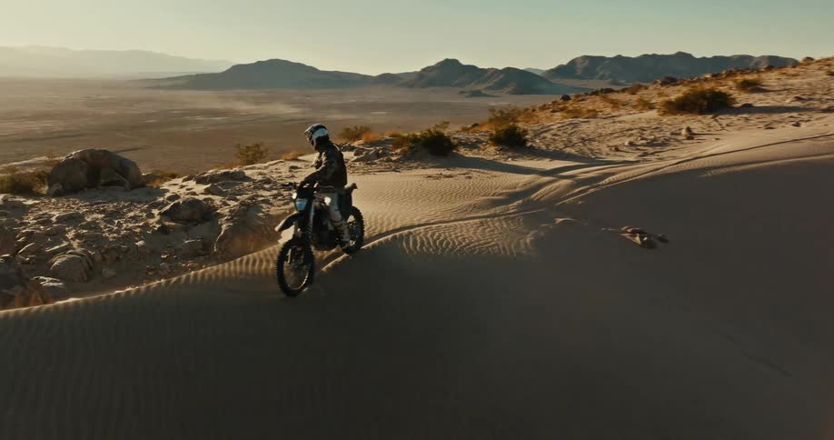 An adventurer sits on his dirt bike and contemplates the vast desert landscape at sunset