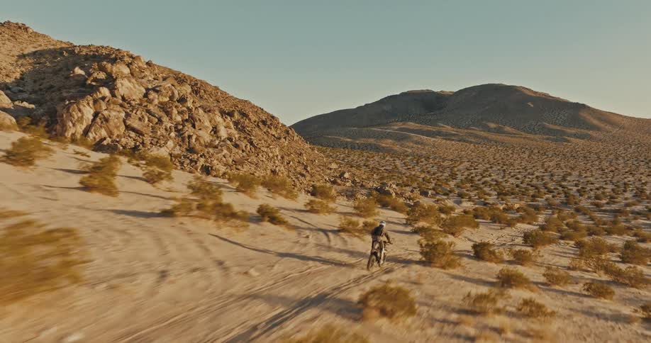 A person rides a motorcycle through desert hills on a clear day