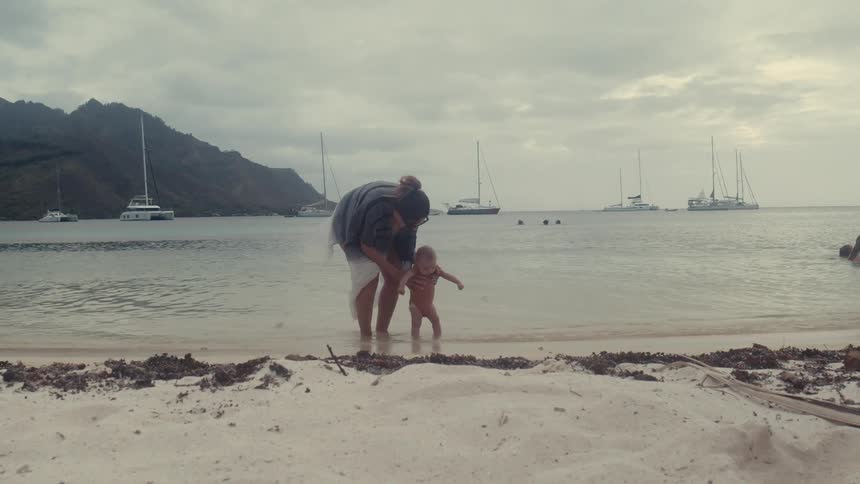 Mother holding her baby daughter with their feet in the sea