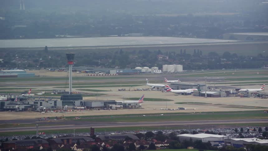 A tower overlooks the runway as planes are parked and others move on the tarmac