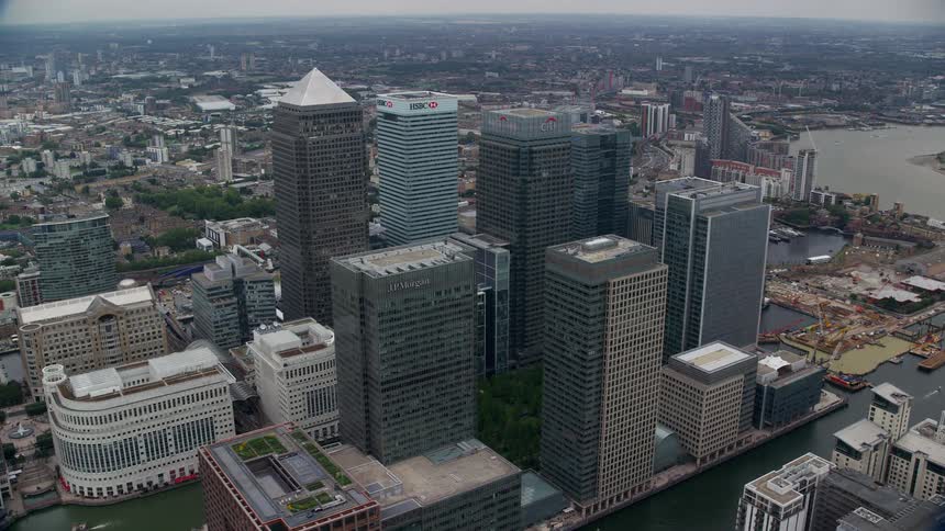 Tall buildings and towers overlook downtown london as ships sail in the harbor and boats are docked in the marina