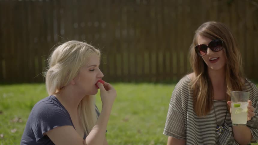 Women sit on a blanket in a yard drinking and eating