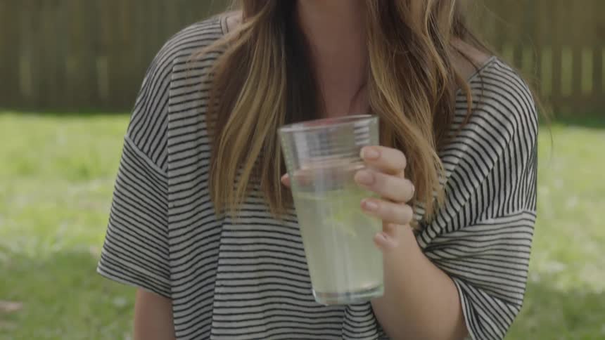 A woman wearing sunglasses is holding a drink and talking