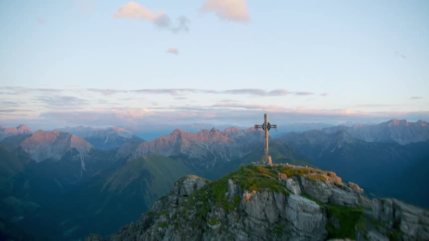 A cross appears at the top of a mountain ridge at sunset
