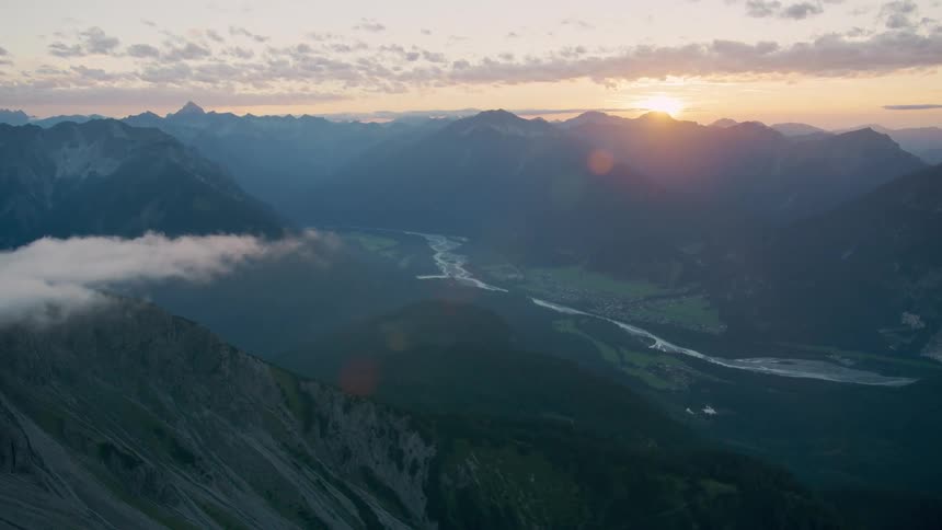 A region with lots of mountains and a river in the middle and the sun shining in the sky