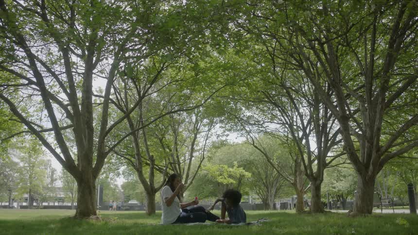 Two people sit down in the grass under some trees