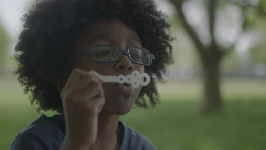 A boy is blowing bubbles on a field