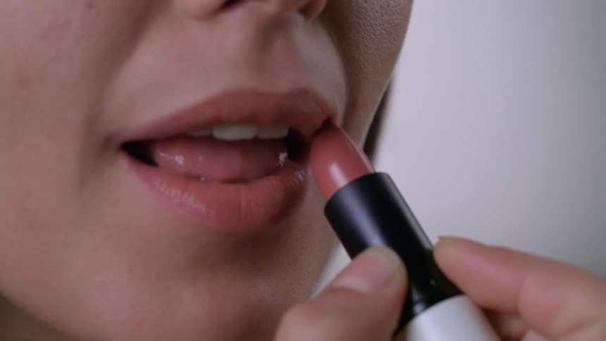 A woman applying pink lipstick to her lips