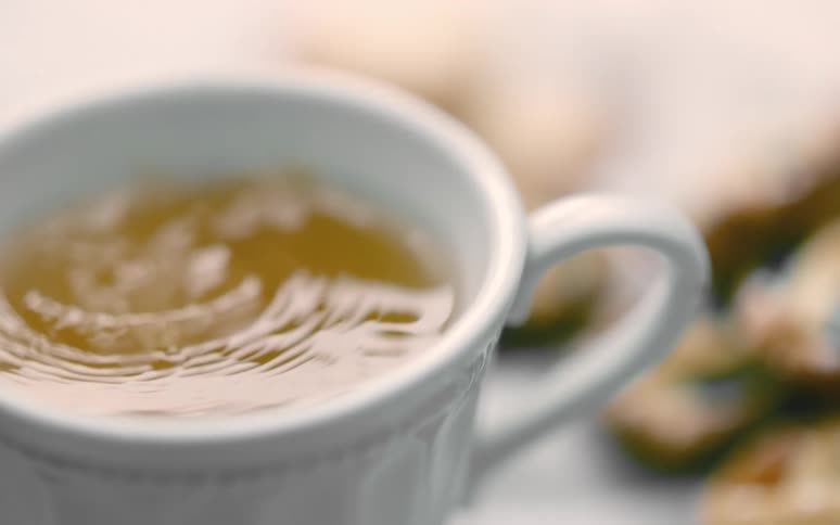Ripples move in a cup of coffee on a table near cookies as sugar falls in