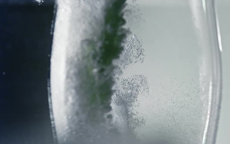 A dark smoky substance moves to the bottom of clear liquid as bubbles rise in a container