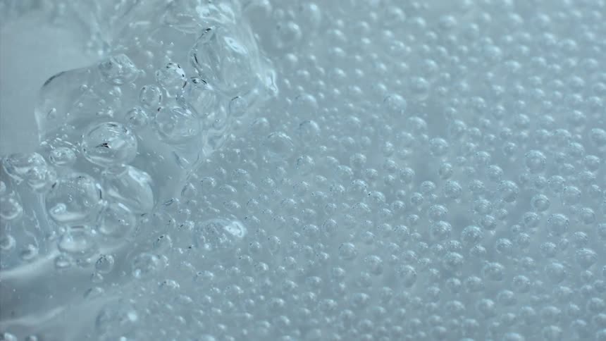A clear blue liquid with several bubbles and a small wave coming from the left