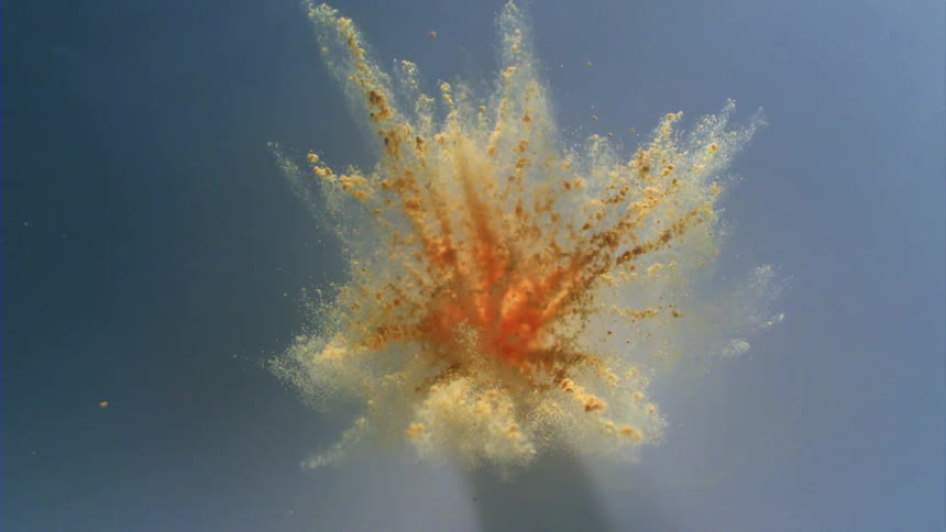 Pale orange particles explode against a blue background