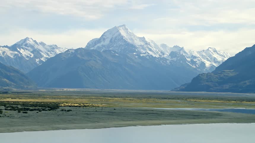 A lake basin sits at the base of a snowcapped mountain range on a cloudy day