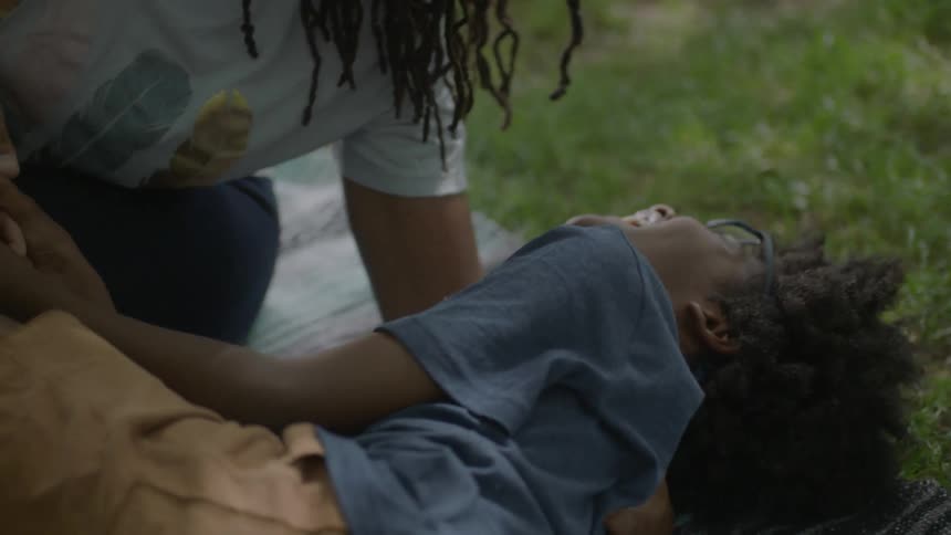 A woman and child play on a blanket in the grass