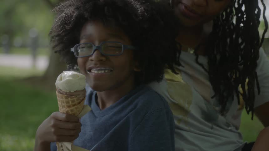 A boy is eating ice cream then looks to this mother smiling