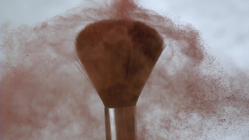 A brush with its bristles full of paint dust moves and throws the dust to the sides