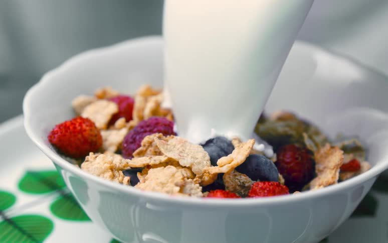Milk being placed on top of the cereal with strawberries in a bowl