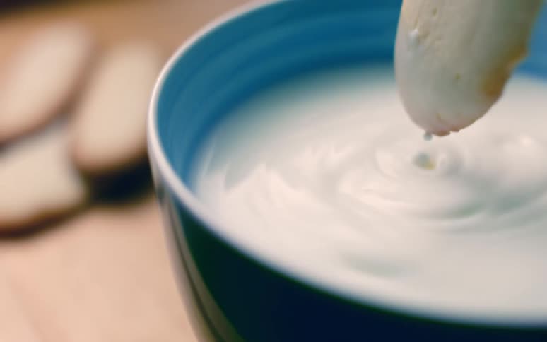 A cookie being dipped in milk in a blue bowl