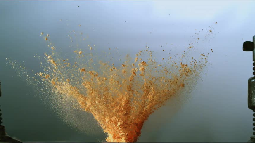 A small explosion in a pile of sand that sends parts flying everywhere