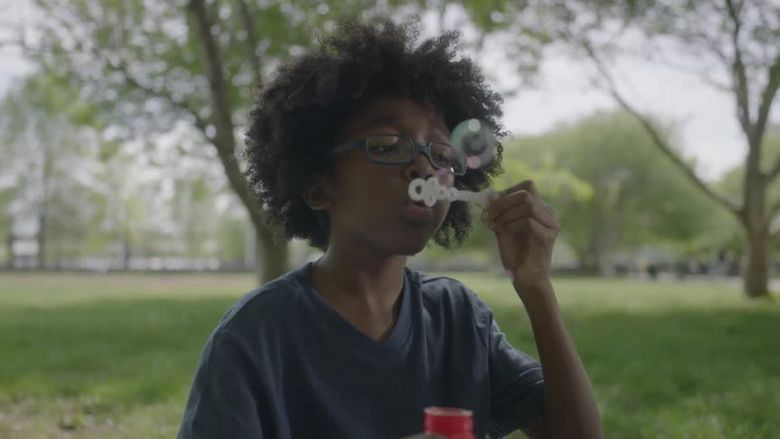 A boy is blowing bubbles on a green field