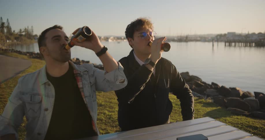 Two friends sitting at a table by a lake having a beer