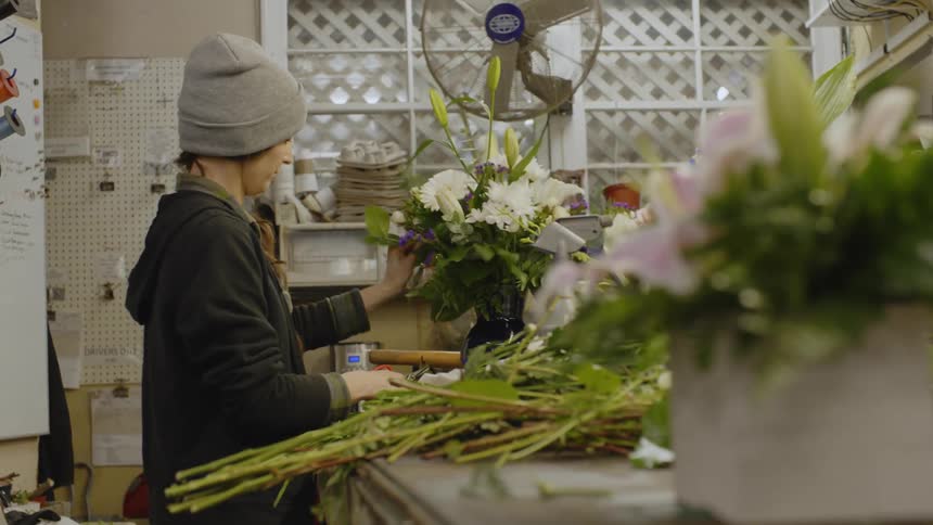 A florist is cutting flowers and putting together a flower arrangement