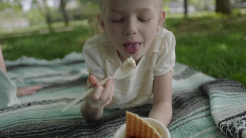 A girl lays on a blanket in the grass eating ice cream