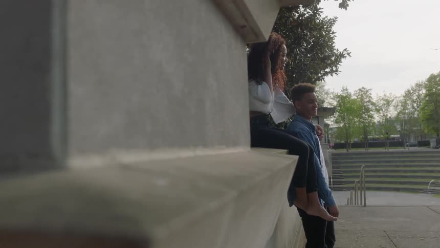 A woman is sitting on a wall with her arm around a man's shoulder below