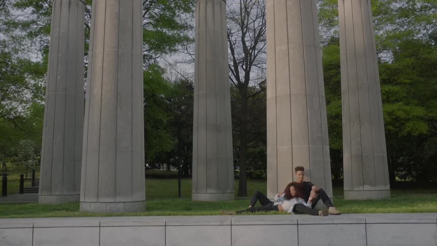 A couple sit together against a pillar on a fall evening