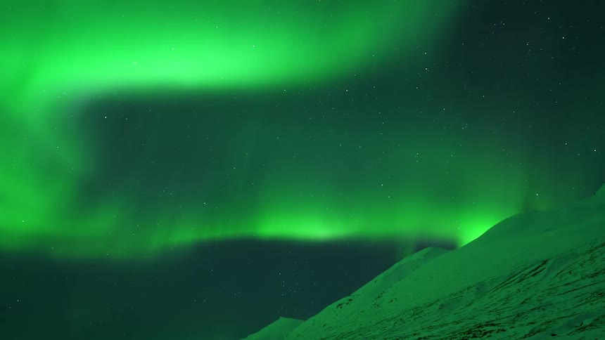 Green lights of the aurora borealis are seen shifting and sweeping dancing around and over a dark sky with mountains in the foreground