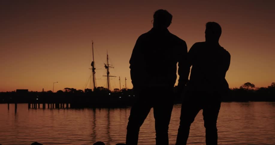 The silhouettes of two men skip rocks at a lake