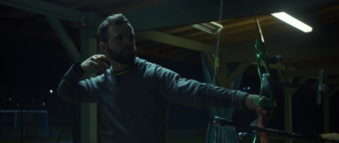 A man uses a bow and arrow to shoot at something at night