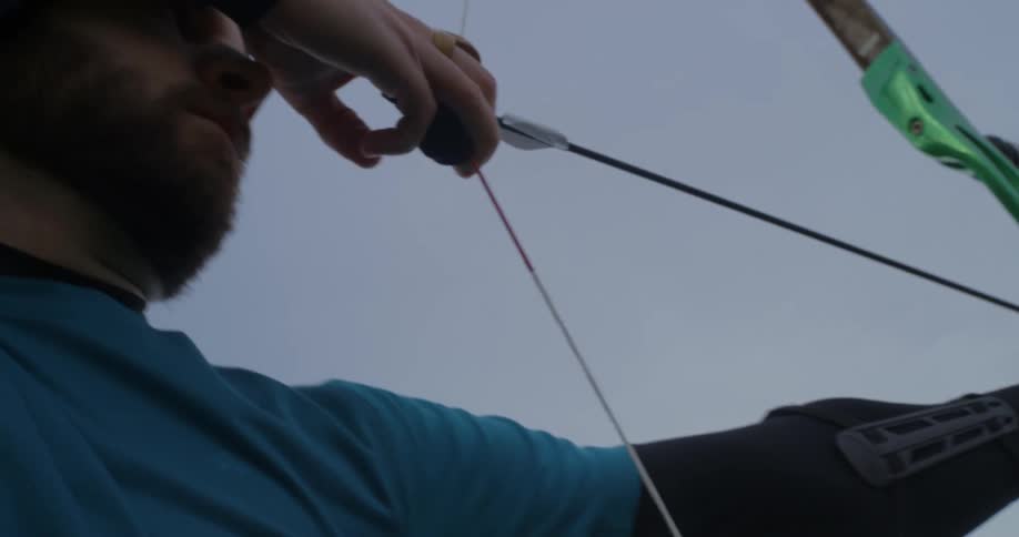 A man with a beard pulling the bowstring with an arrow