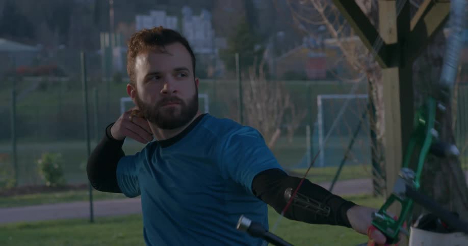 A bearded man shooting an arrow with a sports bow