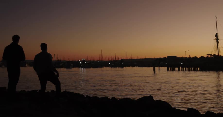 A man throws a rock into the river at sunset