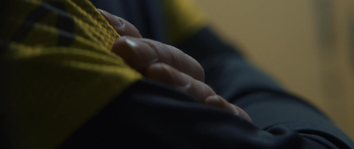 Hands of a person with their arms crossed and wearing black and yellow clothing