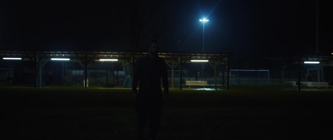 A man walking away from a sports field at night