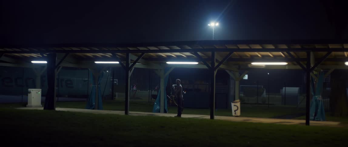 A man is shooting his bow and arrow on a training field while other people play soccer in the background