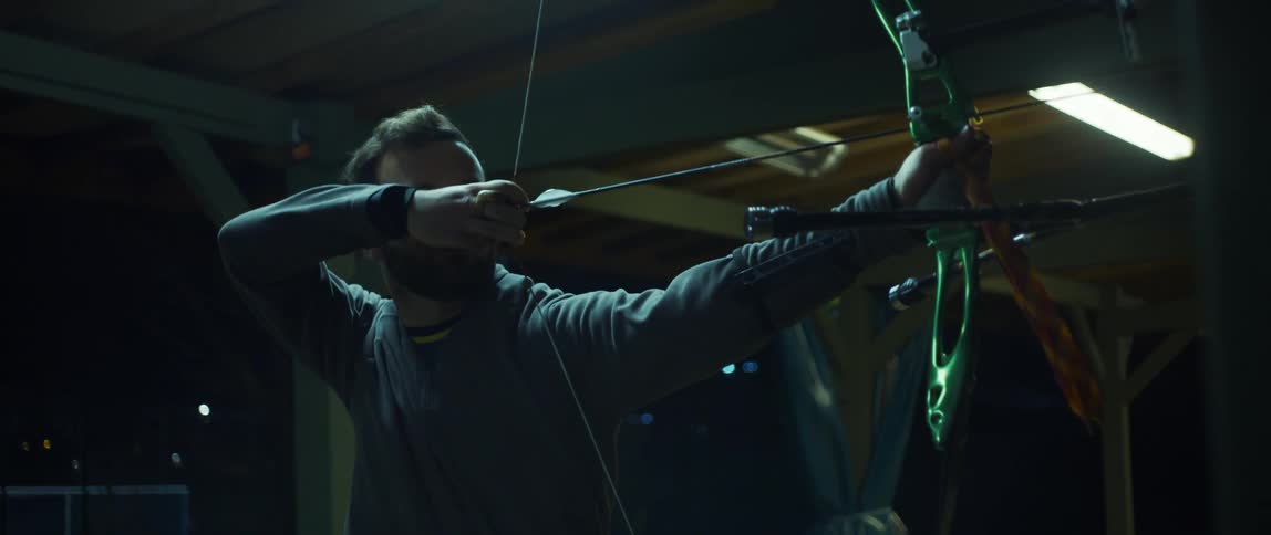 A bearded man pulling a bowstring and aiming